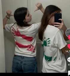 two girls standing next to each other in front of a mirror holding up their hands