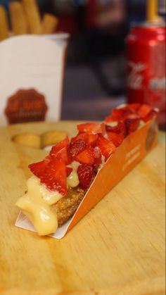 a pastry with strawberries and cheese on it sitting on a wooden table next to a soda