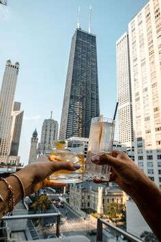 two people toasting with drinks in front of skyscrapers