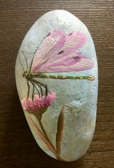 a painted rock with pink flowers and a dragonfly on it's back side