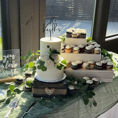 three tiered wedding cake with cupcakes and greenery