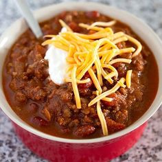 chili with cheese and sour cream in a red bowl on a counter top, ready to be eaten