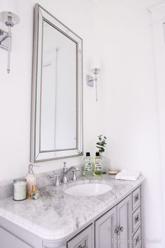 a bathroom with marble counter tops and white walls, along with a large mirror above the sink