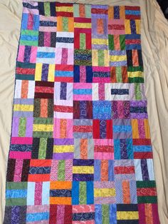 a multicolored quilt is laying on a white bed sheet that has been made with strips of fabric