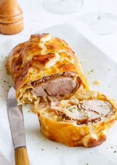 a ham and cheese pastry on a white plate with a knife next to the bread