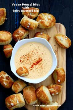 a bowl of dip surrounded by croissants on a cutting board with the words vegan pretzel bites spicy mustard dip