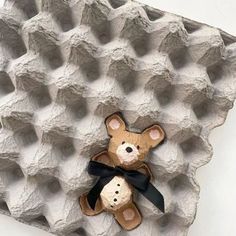 a brown teddy bear sitting on top of an egg carton with black ribbon around its neck