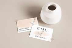 two business cards sitting next to a white vase