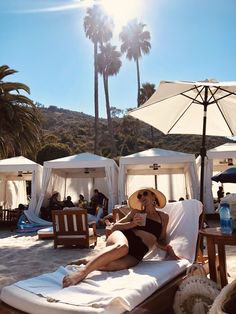 a woman sitting on top of a beach chair under an umbrella next to palm trees