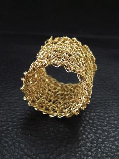 a gold chain ring sitting on top of a black leather surface with an intricate design in the middle