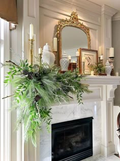 a fireplace mantel decorated with greenery, candles and a mirror on top of it