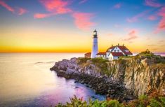 a light house sitting on top of a cliff next to the ocean under a colorful sky