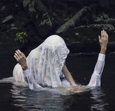 a woman floating in the water wearing a white veil and holding her hands up to her head