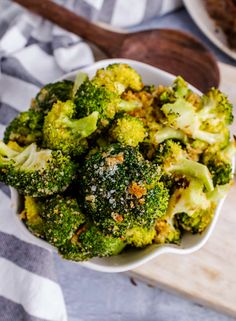 a white bowl filled with broccoli next to an orange and some garlic on a table