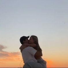 a man holding a woman in his arms as the sun sets behind them and there is no image here to provide a caption for