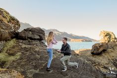 a man and woman standing on rocks near the ocean