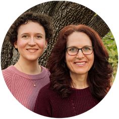 two women standing next to each other in front of a tree