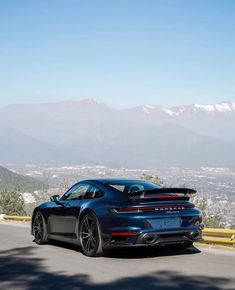 the rear end of a blue porsche sports car driving on a road with mountains in the background