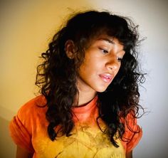 a woman with long curly hair wearing an orange and yellow shirt