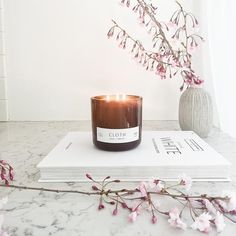 a candle sitting on top of a book next to a branch with pink flowers in it