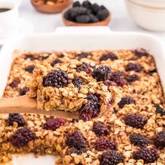 a wooden spoon scooping some granola out of a baking dish filled with berries