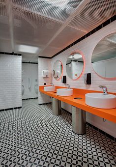 a public bathroom with orange counter tops and white sinks in the center, surrounded by black and white tiles