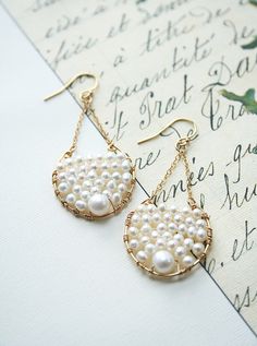 two pairs of earrings with pearls hanging from them on top of a piece of paper