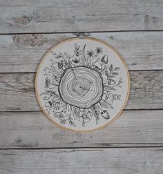 a wooden wall with a cross stitch pattern on it and an embroidery hoop that has a tree stump surrounded by flowers