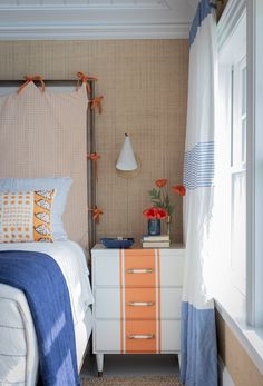 an orange and blue striped dresser in a bedroom with white bedding, pillows and curtains