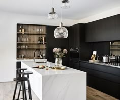 a kitchen with black cabinets and white marble counter tops, two pendant lights hanging from the ceiling