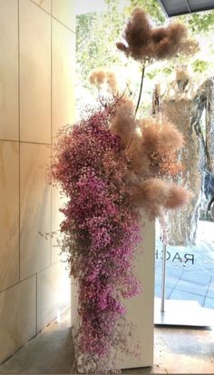 a tall vase filled with purple flowers next to a white pillar covered in dry grass