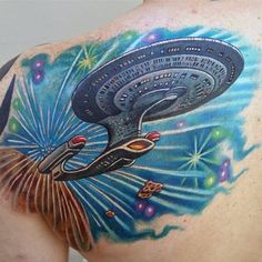 the back of a man's shoulder with a tattoo on it that has an image of a space ship and fireworks