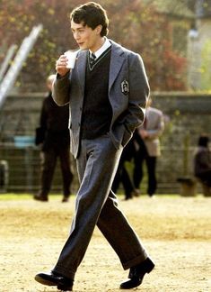 a young man in a suit and tie walking across a field with his hand on his hip