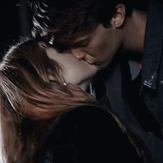 a man and woman kissing in the dark with their hair blowing back to each other