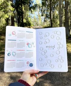 someone is holding up an open planner in the middle of a forest with lots of trees