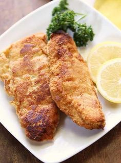 a white plate topped with fried fish next to lemon wedges and broccoli