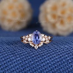 a tan and white ring with an oval blue sapphire surrounded by smaller round diamonds on a blue cloth