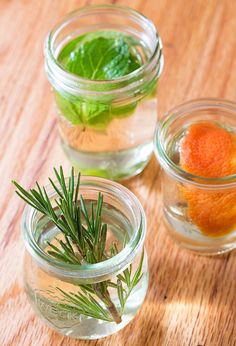 three jars filled with water and herbs on top of a wooden table next to each other