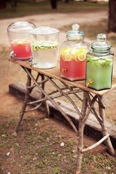 three jars filled with drinks sitting on top of a wooden table next to a tree