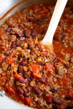 a large pot filled with chili and meat next to a wooden spoon in the bowl