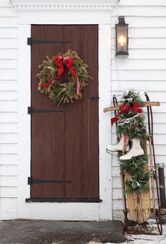 a white house with a wreath and snow shovels on the front door, next to a sled