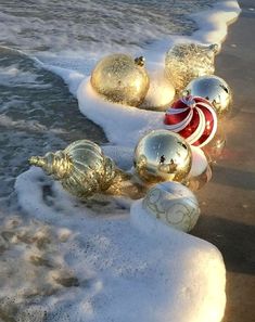 christmas ornaments are lined up on the beach in front of the water and snow covered shore