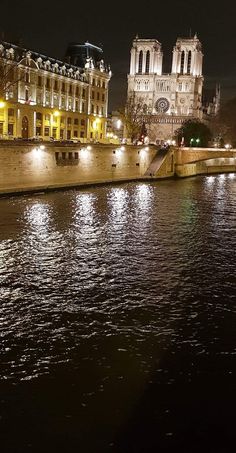 the lights are on in front of the buildings along the water's edge at night