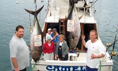 a group of people standing on the back of a boat holding up two large fish