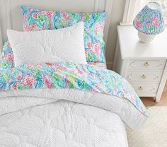 a white bed with colorful comforter and pillows