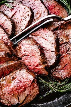 sliced steak on a plate with rosemary garnish next to a knife and fork