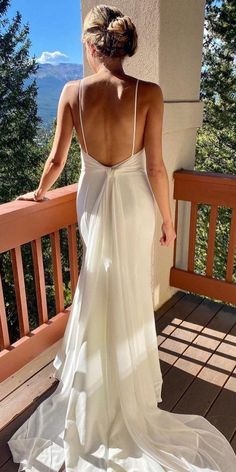 a woman in a white dress standing on a balcony looking out at the mountains and trees