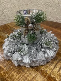 a candle holder decorated with pine cones and silver ornaments on a wooden table in front of a white wall