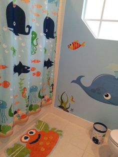 a bathroom decorated in blue and orange with an ocean theme on the shower curtain, toilet seat cover and rug