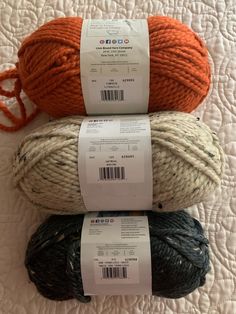 three balls of yarn sitting on top of a white bed sheet with orange and black stripes